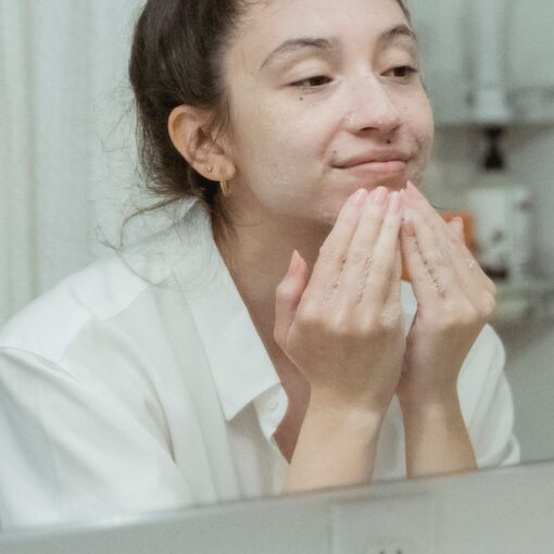 Young woman washing her face with foamy cleanser, reflected in a bathroom mirror, skincare routine